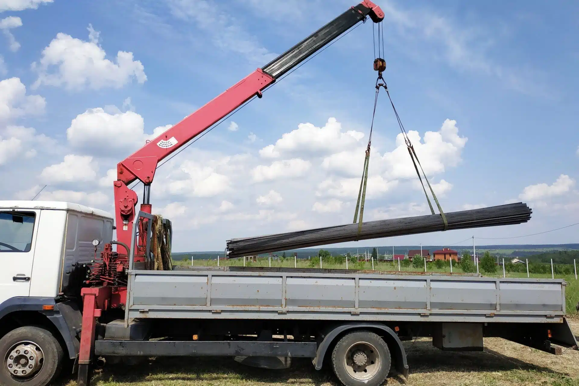 The truck crane in the field on the private land unloads the metal profile.